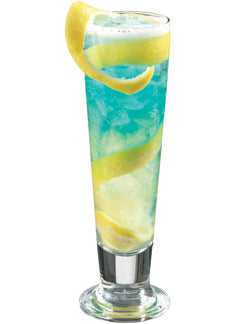 A bright blue and yellow cocktail with ice is served in a tall glass with a long lemon peel garnish wrapped around the glass and a lemon wedge on the rim