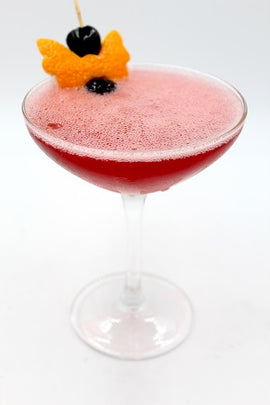 Coupe glass with red drink orange peel cherry plain background