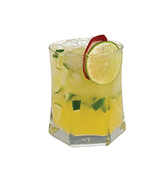A pale yellow cocktail with ice is served in a short glass with lime slices and fresh mint pieces visible inside, garnished with a lime slice on the rim