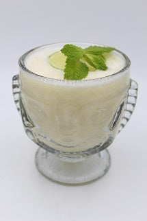 Tiki glass with creamy white drink lime slice mint sprig plain background