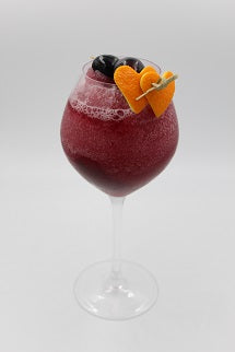 Red berry drink in a glass garnished with blueberries and an orange slice