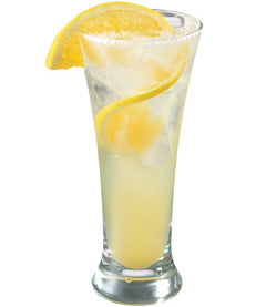A pale yellow lemon cocktail with ice is served in a tall glass with lemon slices visible inside and a large lemon wedge on the rim