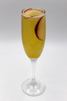 A golden yellow cocktail is served in a tall stemmed glass with a peach slice visible inside and a peach garnish on the rim.