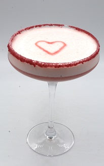 A coupe glass filled with a pink foam drink decorated with a red heart on a plain background