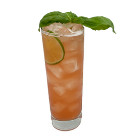 A pink-orange cocktail with ice is served in a tall glass with a lime slice inside and fresh basil leaves arranged across the top.