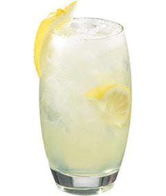 A pale yellow lemon cocktail with ice is served in a tall rounded glass with lemon slices visible inside and a curled lemon peel garnish on the rim