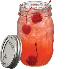A red cocktail with crushed ice and several cherries is served in a mason jar with the lid placed beside it