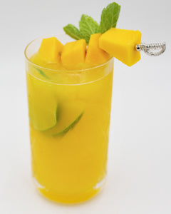 Yellow mango cocktail with ice lime pieces and mint garnish in a tall glass