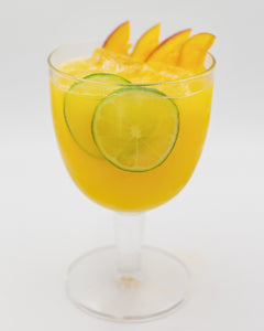 A bright yellow cocktail is served in a rounded stemmed glass with lime slices visible inside and several orange slices arranged on top