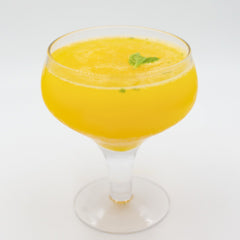 A bright yellow cocktail with ice is served in a coupe glass and garnished with a small fresh mint leaf on the surface.