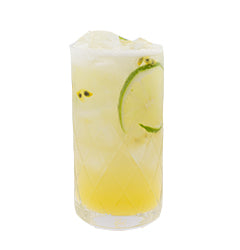 A pale yellow cocktail with ice is served in a tall glass with a lime slice visible inside and small passion fruit seeds scattered throughout