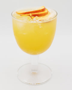 A bright yellow cocktail with ice is served in a rounded stemmed glass and garnished with several orange slices on top.
