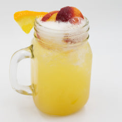 A pale yellow cocktail is served in a mason jar with a foamy top and garnished with orange and red fruit slices.