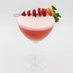 A pink cocktail with a thick white foamy top is served in a coupe glass and garnished with sliced strawberries and a whole strawberry with green leaves on top.