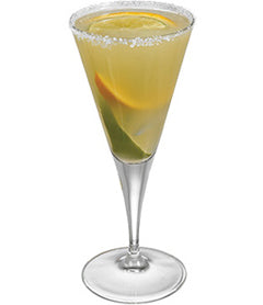 A pale yellow citrus cocktail is served in a tall stemmed glass with a salted rim and lime and orange slices visible inside.