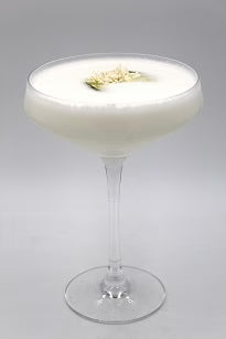 Coupe glass with creamy white drink white garnish plain background