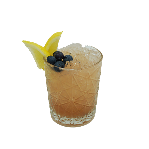 A peach-colored cocktail with crushed ice is served in a patterned short glass and garnished with blueberries and two lemon wedges